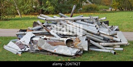 A pile of old galvanized rain drain pipes lies on green  grass Stock Photo