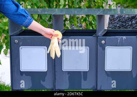 Woman throws medical gloves in the trash on the background of trees in the park Stock Photo