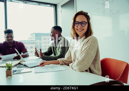 Beautiful business woman smiling wearing glasses sitting with partners around table in conference room Stock Photo