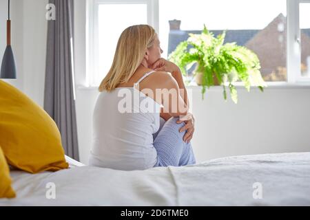 Unhappy Mature Woman Suffering With Depression Sitting On Bed Wearing Pyjamas