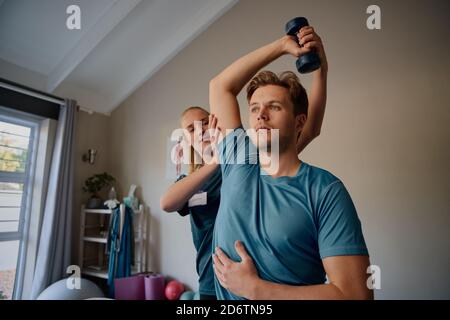 Physiotherapist instructing male patient correct exercise form with dumbbells Stock Photo