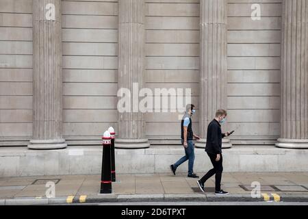 People wearing face masks pass the columns of the Bank of England in the City of London financial district which is still very quiet with few people around and working due to the Coronavirus outbreak as lockdown continues on 9th September 2020 in London, United Kingdom. Stock Photo