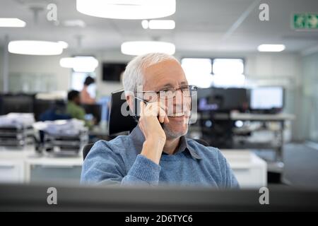 Senior businessman talking on smartphone while sitting on his desk at modern office Stock Photo