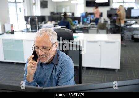 Senior businessman talking on smartphone while sitting on his desk at modern office Stock Photo