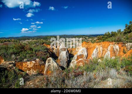 Eroded stone landscape with red soil and vegetation under blue sky wit Stock Photo