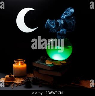 Halloween concept. Glass transparent bowl with steamed green liquid stands on top of books pile, covered with web. Stock Photo