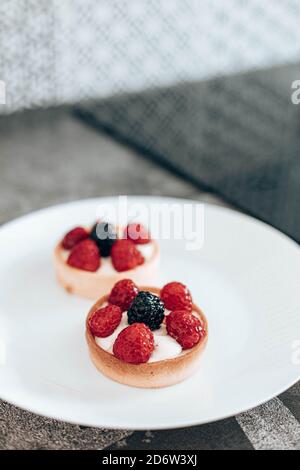 Delicious tartlets or cake with mixed berry on white plate in the kitchen. Summer pastry desserts. Vertical photo orientation Stock Photo