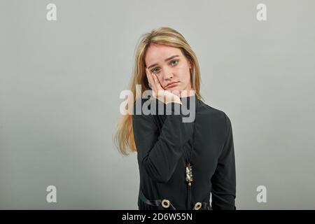 Holding hand on cheek, resting face in hands, offended displeased looks with moody expression keeps fingers countenance stands upset. Negative expressions and feelings concept. Isolated shot Stock Photo