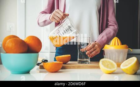 Caucasian woman in casual clothes is pouring juice in a glass after squeezing from lemons and oranges Stock Photo