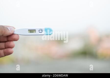 Sick man holds digital thermometer with body temperature reading in Fahrenheit up close to the camera. Stock Photo