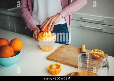 Close up photo of a caucasian woman squeezing fresh juice out of sliced oranges in the kitchen Stock Photo
