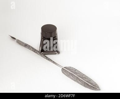 Old ink pen with metal filigreed and ink bottle isolated on white background. Vintage calligraphy pen and bottle of ink. Stock Photo