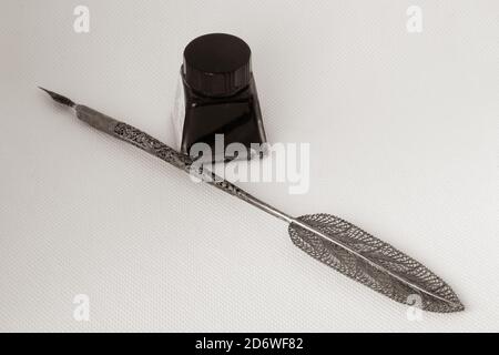 Old ink pen with metal filigreed and ink bottle isolated on white background. Vintage calligraphy pen and bottle of ink. Stock Photo