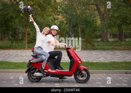 Happy young love couple on retro red scooter outdoors. Romantic dating in the park Stock Photo