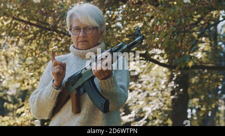 Elderly gray haired woman holding a gun in her hands. War or revolution concept. High quality photo Stock Photo