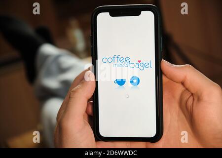 CoffeeMeetsBagel white logo on the screen of mobile phone in mans hand. Application for dating and acquaintance. Man is laying on the sofa and looking Stock Photo