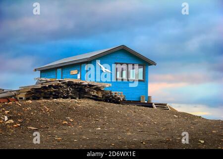 Picturesque arctic view - blue colored wooden house with white seagull on the barren tundra ground and dramatic cloudy sky in Longyearbyen, Norway Stock Photo