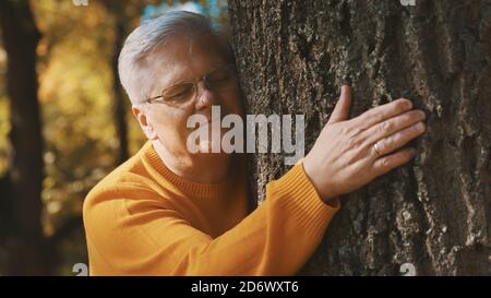 An older man lovingly hugging and leaning face to tree trunk feels relaxed and good on the autumn day. High quality photo Stock Photo