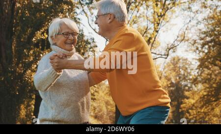 Happy old couple dancing in park. Senior man flirting with elderly woman. Romance at old age autumn day. High quality photo Stock Photo