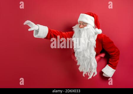 Santa man breaks through hole in paper like super man. Space for text. Holiday poster design, banner. Stock Photo