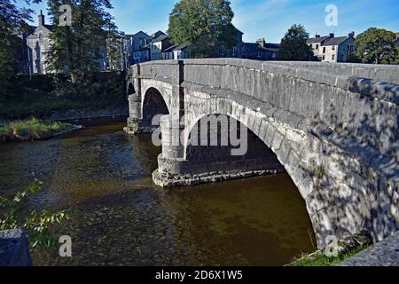 Miller Bridge or Mill Bridge in Kendal town centre, Cumbria, England. The River Kent flows through the stone arches. Traditional buildings on the bank. Stock Photo