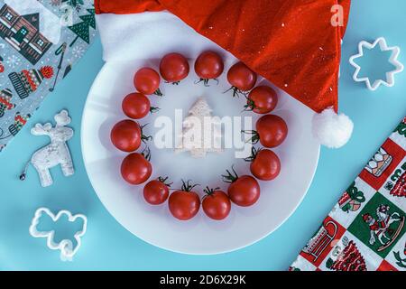 Xmas, winter, new year concept - layout white plate on which there are Christmas tree carved from bread and surrounded red cherry tomatoes with santa Stock Photo
