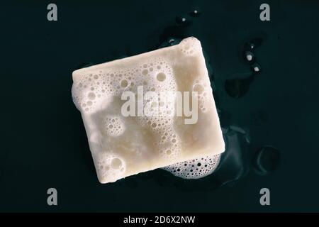 Soap bar natural diy olive oil foaming with foam bubbles texture on black background .Top view. Washing hands with soap for personal hygiene Stock Photo