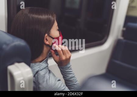 Mandatory face covering in public transport during coronavirus pandemic. Woman commuter putting on cloth mask. Passenger touching mouth cover on Stock Photo