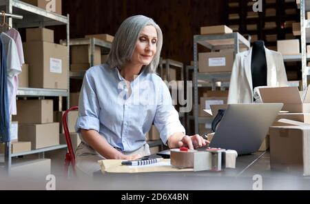 Mature female seller using computer checking ecommerce clothing orders. Stock Photo