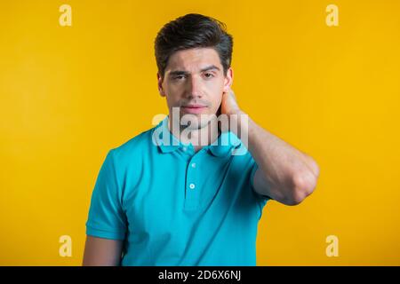 Young man having pain in neck, studio portrait. Guy putting hands on throat, isolated on yellow background. Concept of problems, medicine, illness Stock Photo
