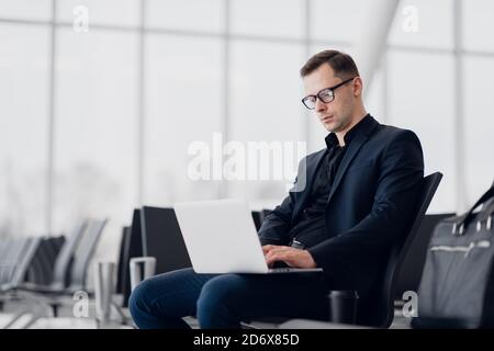 Young business man sitting on the computer with modern stylish wireless earphones at the airport waiting for the flight Stock Photo