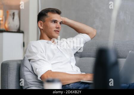 thoughtful young man with a laptop sitting on the couch. Stock Photo
