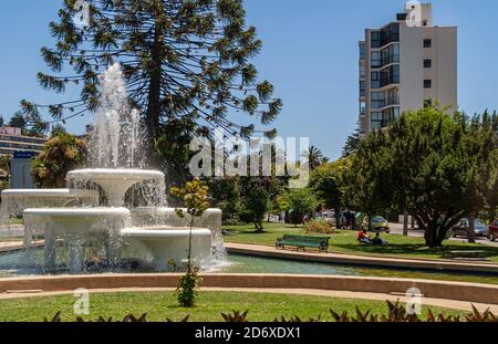 Vina Del Mar, Chile - December 8, 2008: Big white fountain in green park of Plaza Mexico with tall building on side. Trees, lawns and a few people. Stock Photo