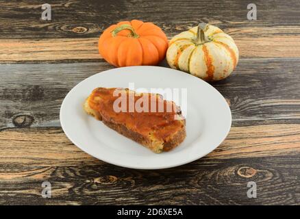 Pumpkin butter on slice of bread on white bread plate and pumpkins on table Stock Photo