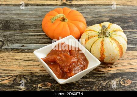 Pumpkin butter in white bowl and fresh small pumpkins on table Stock Photo