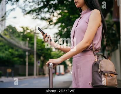 Businesswoman on side of road using smartphone, using app to book a cab, communication, connection, on the move, business travel Stock Photo