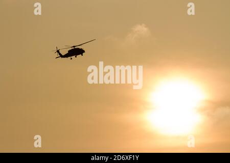 A silhouetted Sikorsky SH-60 Seahawk helicopter, of Carrier Air Wing Five, flying in front a cloudy sunset, Kanagawa, Japan. Stock Photo