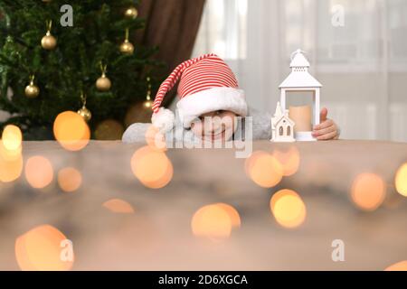 A child in a New Year's cap, lies on his palm in a hug with a lamp house and smiles broadly lips.  Stock Photo