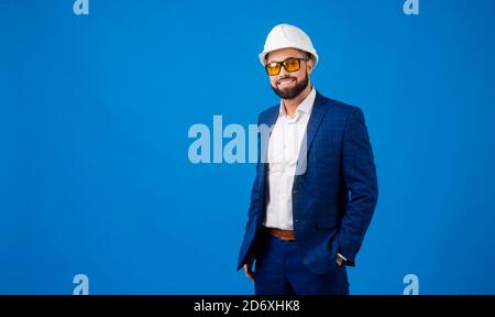 A young professional wearing a hard hat and carrying a clipboard on blue background Stock Photo