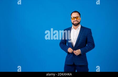 Young man wearing sunglasses in a classic blue suit on a blue background Stock Photo
