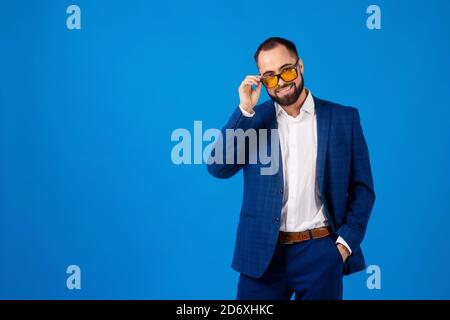 Young man wearing sunglasses in a classic blue suit on a blue background Stock Photo