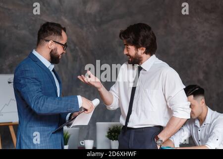 Diverse friendly male partners colleagues talking walking in modern office hallway, young african american and caucasian business men discussing Stock Photo