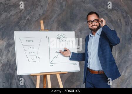 Confident middle-aged Caucasian businessman talk explain business plan presenting project on flip chart, male coach or trainer in glasses make Stock Photo
