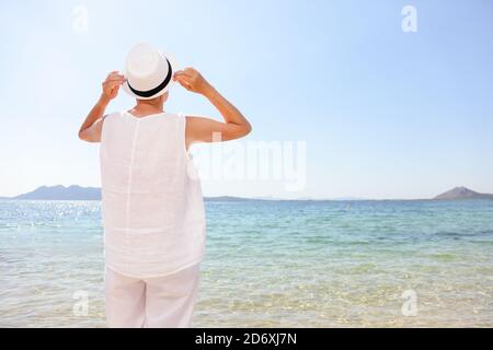 Senior happy woman retired enjoying sun wearing hat on Caribbean beach vacation. Travel tourist standing at sea and clear sky. Rear view of female in Stock Photo