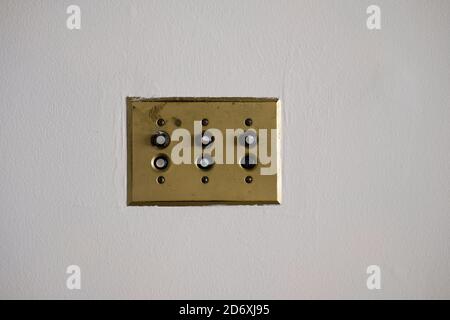 H&H Arrow single pole push light switches mounted on a brass plate on a white wall; manufactured in the 1930s by Arrow-Hart & Hegeman Electric Co. Stock Photo