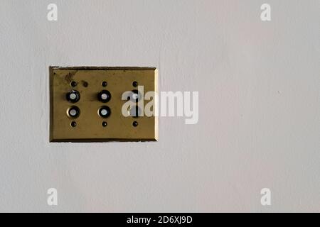 H&H Arrow single pole push light switches mounted on a brass plate on a white wall; manufactured in the 1930s by Arrow-Hart & Hegeman Electric Co. Stock Photo