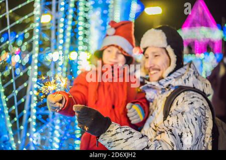 Little boy and his father with sparklers near giant fir tree and Christmas illumination on Christmas market. Xmas holidays on fair Stock Photo