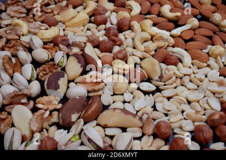 A lot of various nuts on dark blue metal deck: peanuts, cashews, hazelnuts, Brazil nuts, almonds, pistachios, walnuts, popularity as man’s best, close Stock Photo