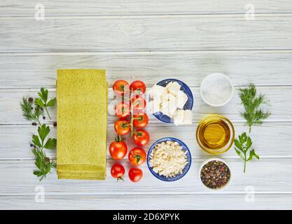 Sheets for making lasagna with spinach and ingredients: cherry tomatoes, cheese, butter, peppers and herbs. Food knolling, top view. Stock Photo