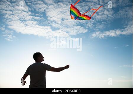 young active male with flying multicolored kite on sea and blue sunset sky background Stock Photo